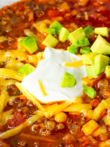 Close-up of a hearty meatless vegetarian chili bowl with toppings like shredded cheese, sour cream, and fresh avocado, perfect for game day or a cozy meal.