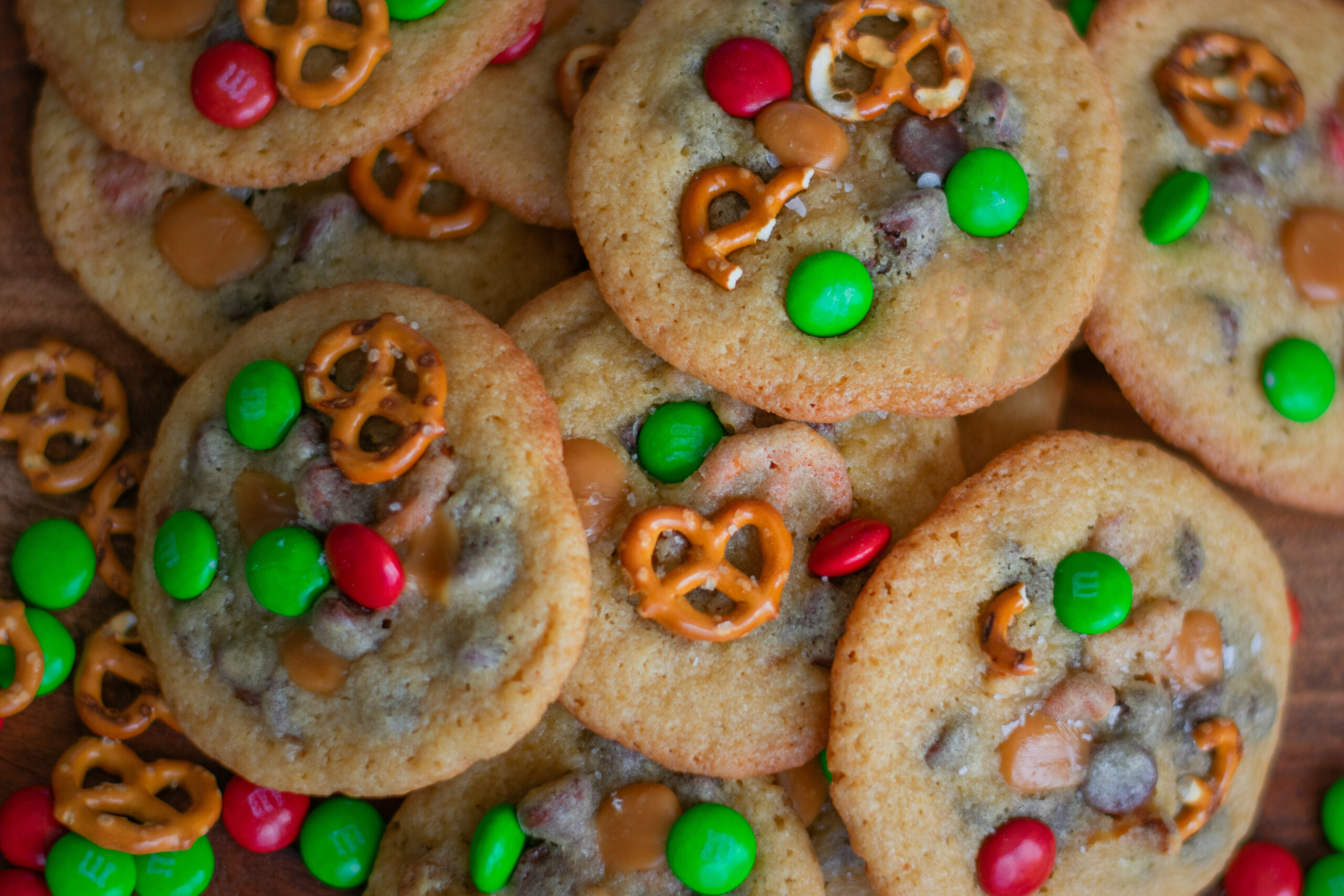 Festive Kitchen Sink Cookies loaded with chocolate chips, pretzels, holiday candy, and more on a red and white stripe, perfect for holiday parties and cookie swaps.