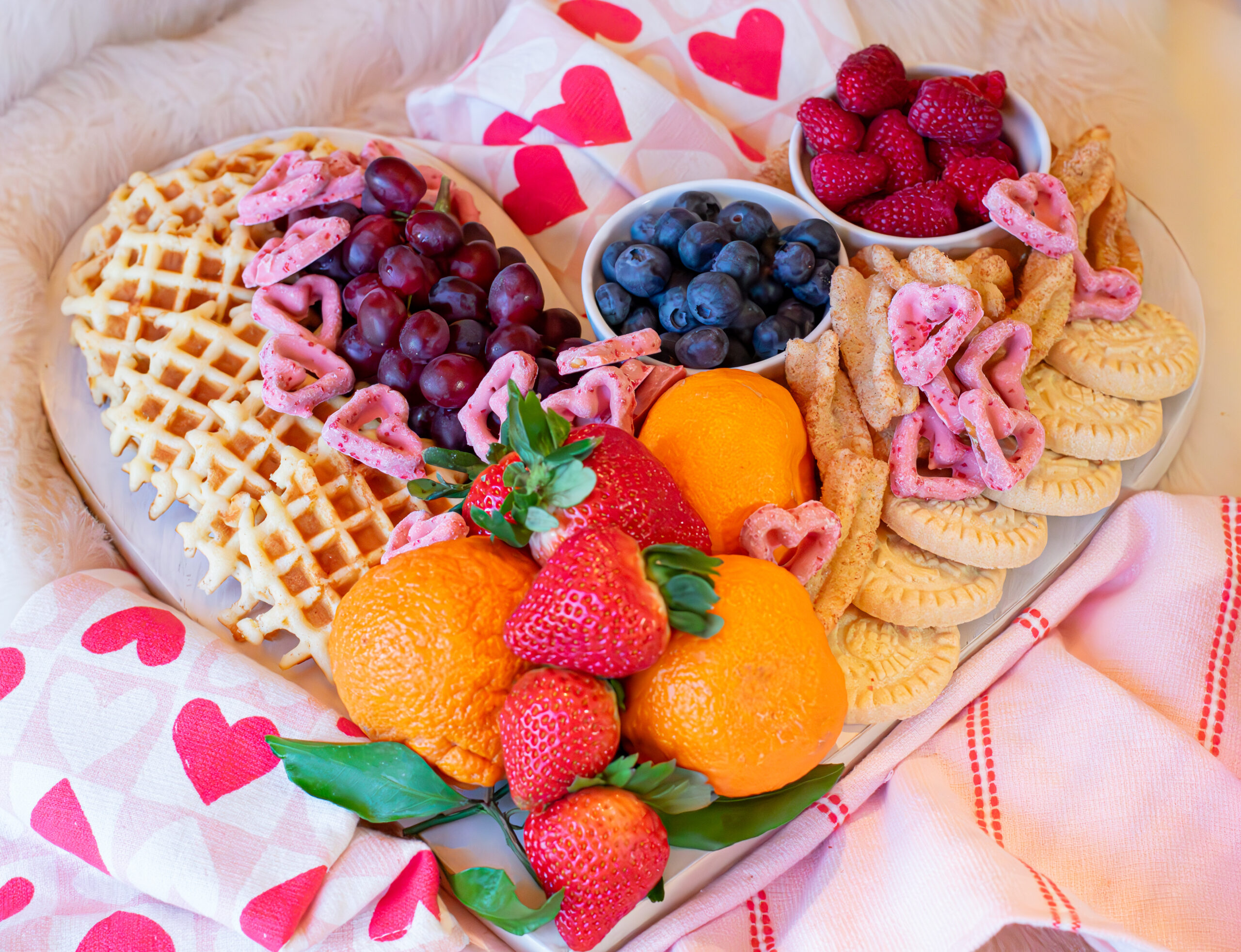 Romantic Valentine’s Day brunch spread, fresh berries, heart shaped chocolate-pretzel strawberries, cookies, and belgian waffles.