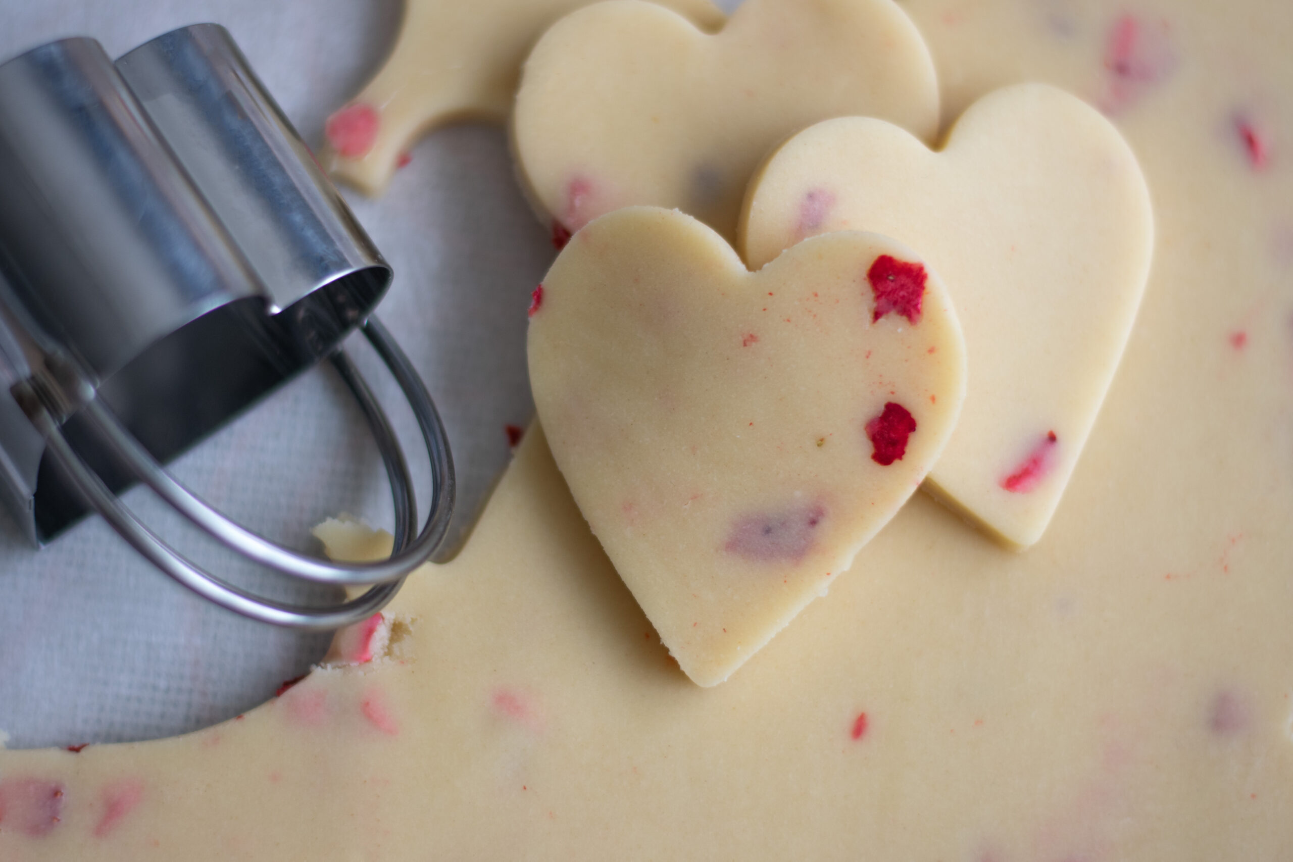 Strawberry Flecked Shortbread Cookie Dough with heart-shaped cookies cut out on top with cookie cutter