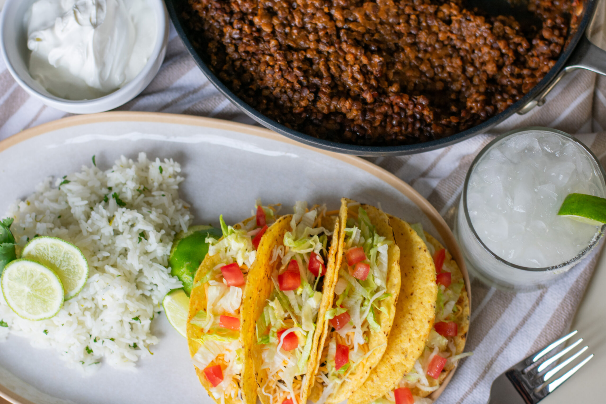 Vegetarian tacos served alongside flavorful lentil filling, topped with crisp lettuce and fresh tomatoes, with a refreshing margarita on the side.