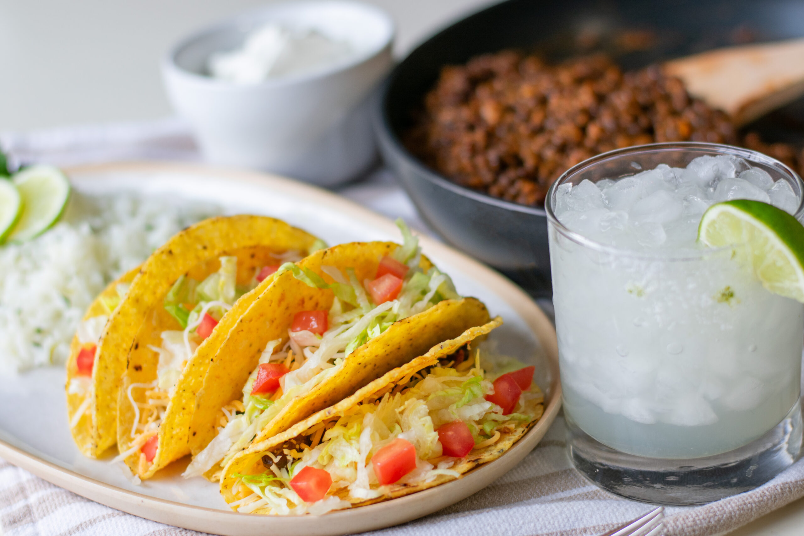 Vegetarian tacos served alongside flavorful lentil filling, topped with crisp lettuce and fresh tomatoes, with a refreshing margarita on the side.