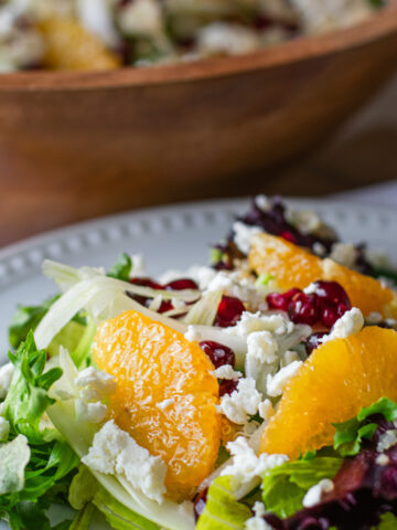 Vibrant citrus fennel salad with pomegranate gems served in a large acacia wood bowl, showcasing fresh, colorful ingredients and a homemade vinaigrette