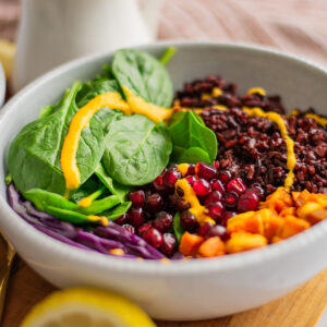 Winter Glow Buddha Bowl with black rice, roasted sweet potatoes, pomegranate seeds, and a drizzle of tangy dressing. A colorful and healthy meal for mindful eating.