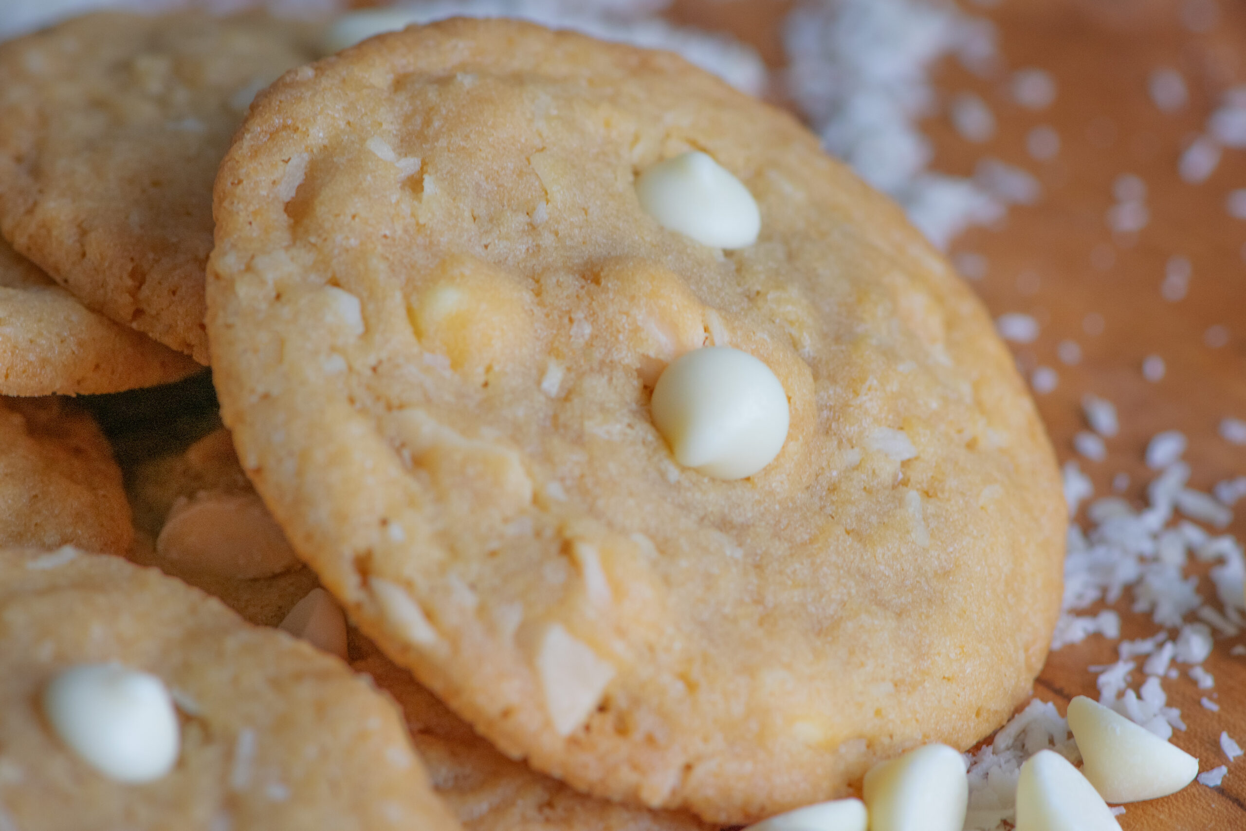 Close-up of coconut cookies with a golden caramelized edge, featuring white chocolate and shredded coconut.