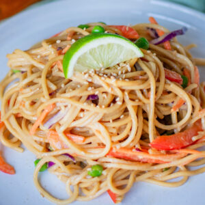Cold vegetable lo mein noodles topped with lime and fresh veggies on a plate
