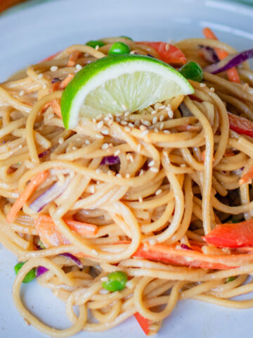 Cold vegetable lo mein noodles topped with lime and fresh veggies on a plate
