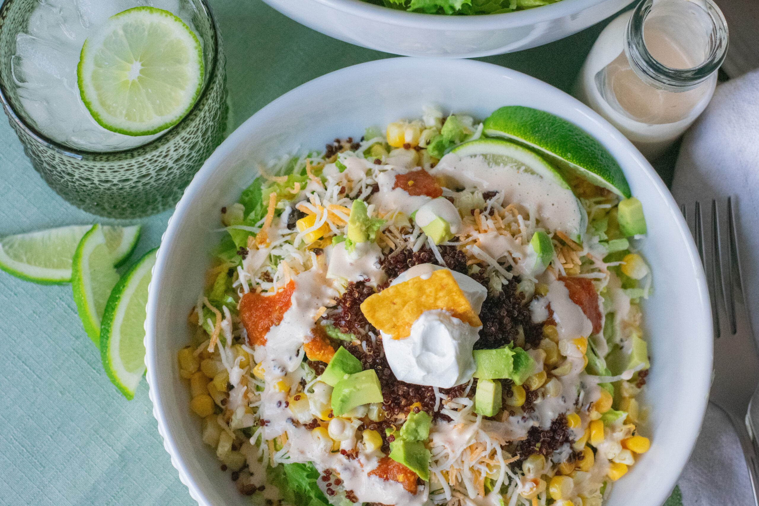 Overhead view of a colorful vegetarian taco salad with crispy red quinoa, grilled corn, avocado, shredded cheese, and creamy spicy dressing.