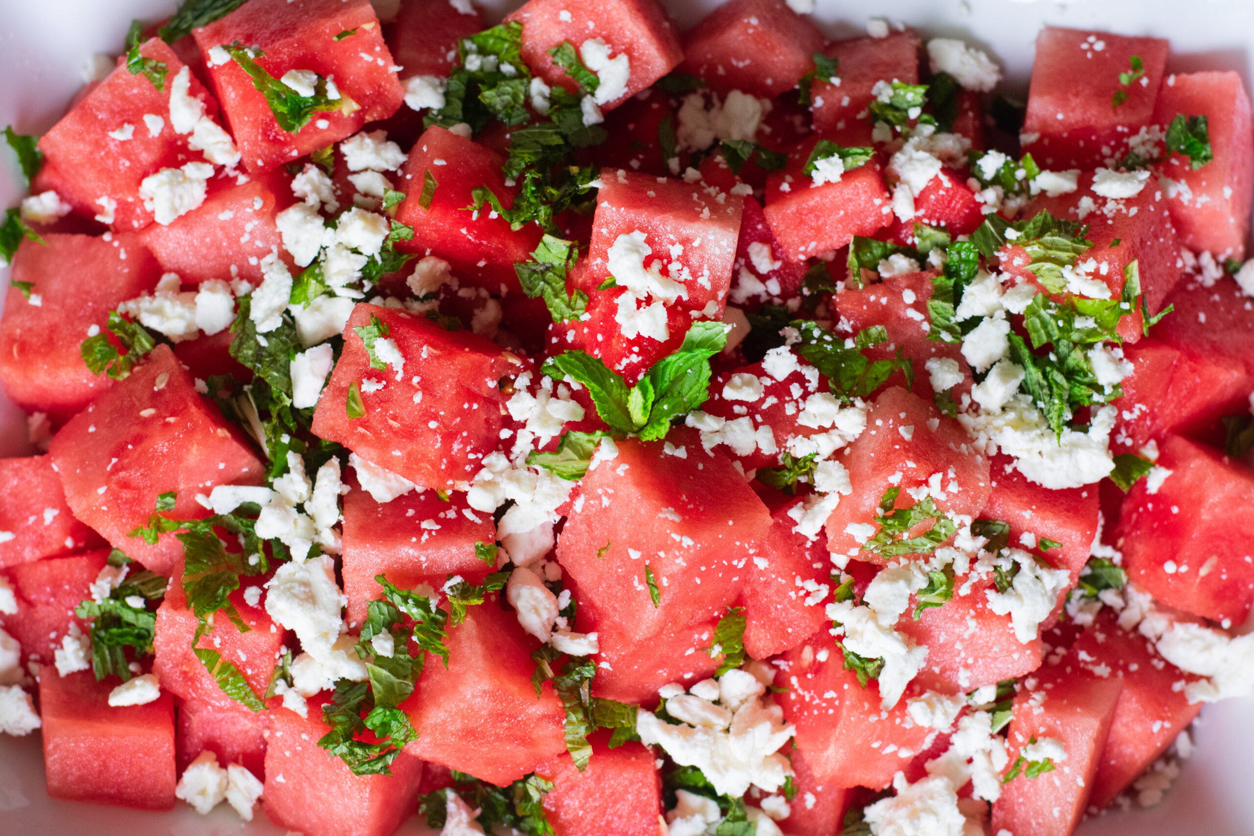Top-down shot of a vibrant watermelon salad with crumbled feta, fresh mint leaves, and lemon dressing