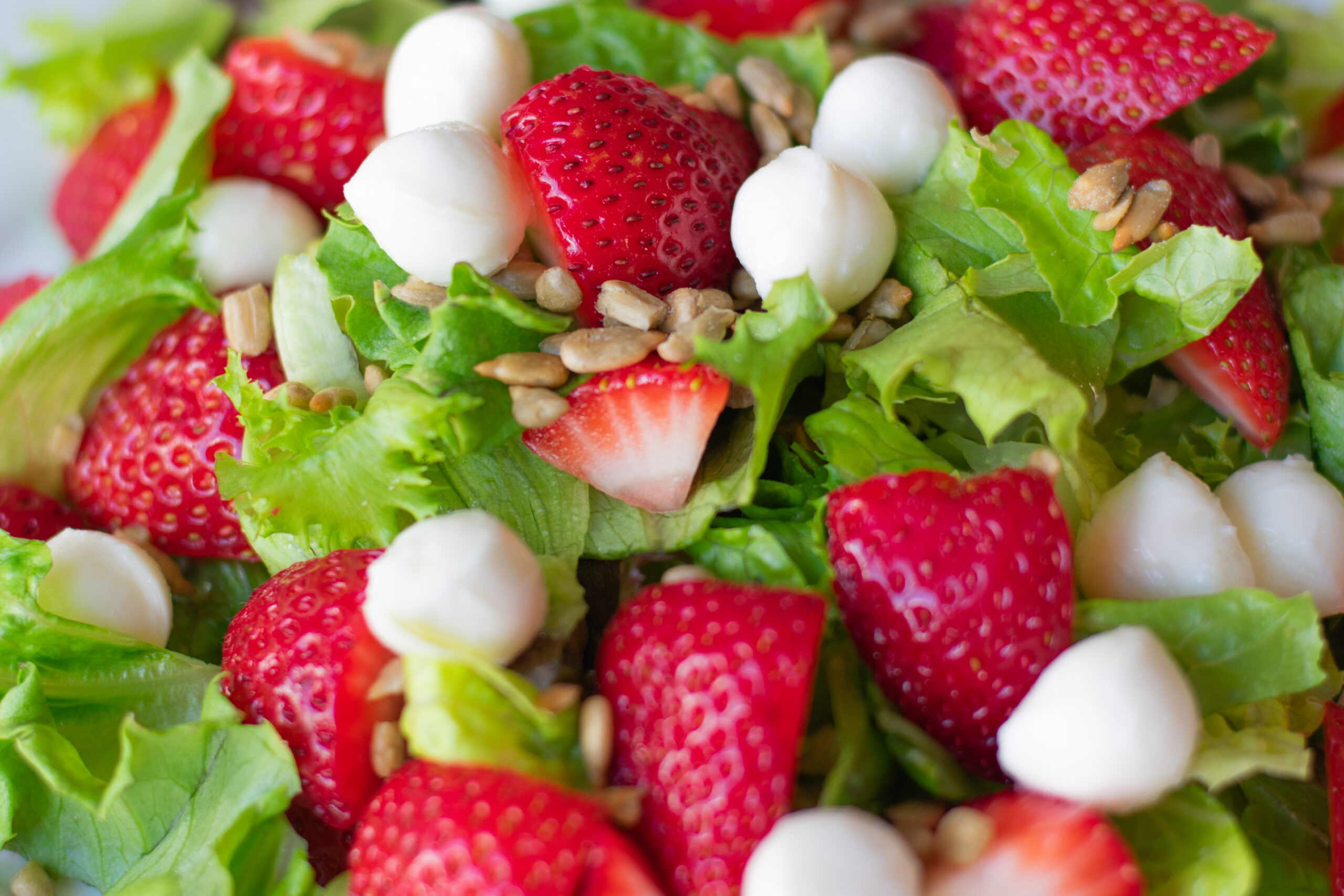 Close-up of strawberry caprese salad featuring fresh strawberries, mozzarella balls, romaine and mixed greens, and crunchy sunflower seeds without dressing.