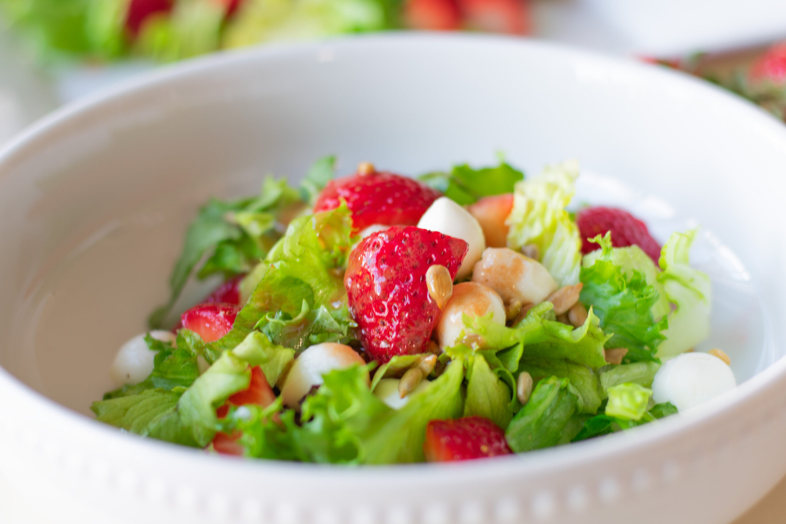 Bowl of strawberry caprese salad with fresh strawberries, mozzarella balls, mixed greens, and sunflower seeds tossed in creamy strawberry vinaigrette.
