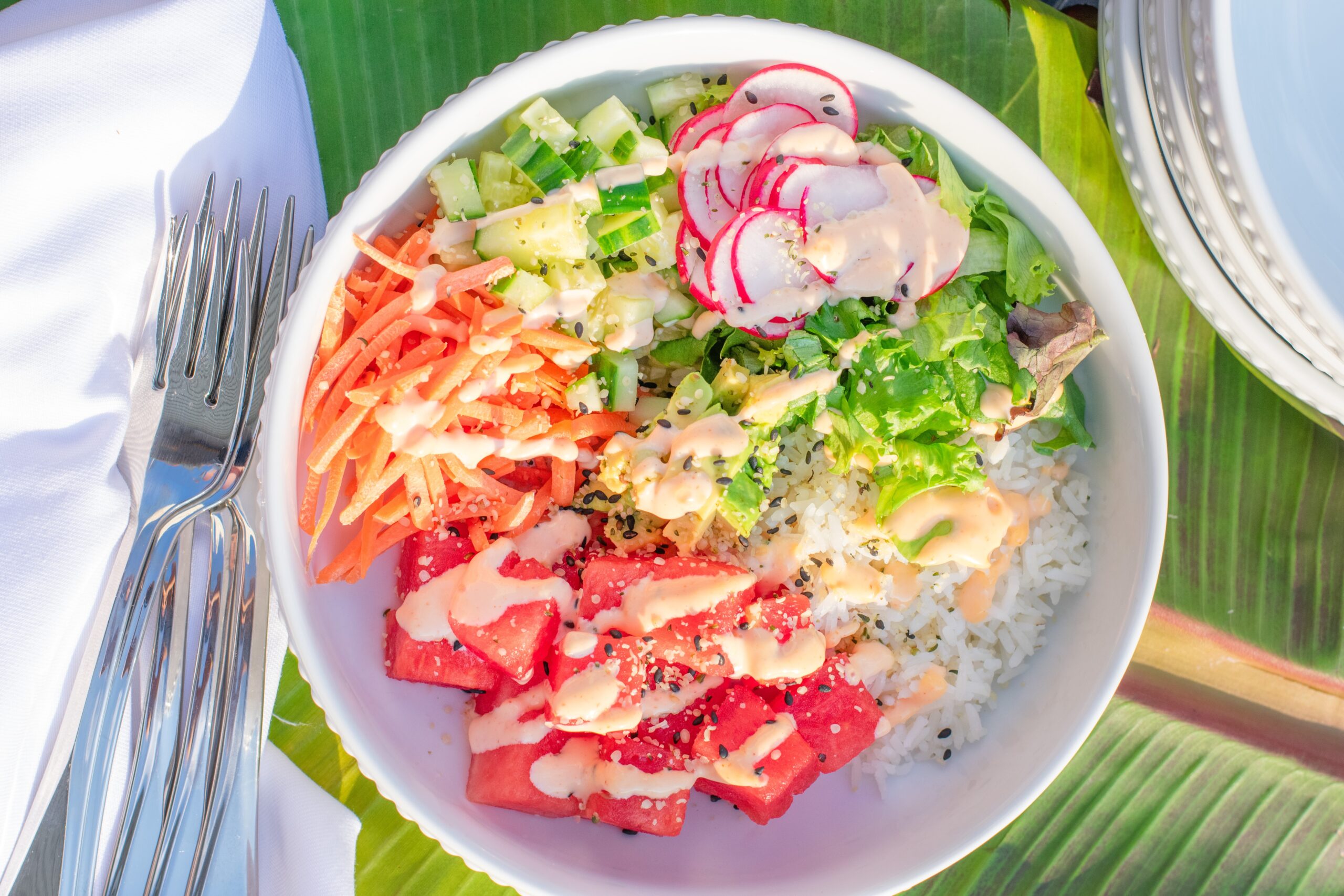 Colorful vegetarian poke bowl served with stacked bowls and a fork on a tropical banana leaf background