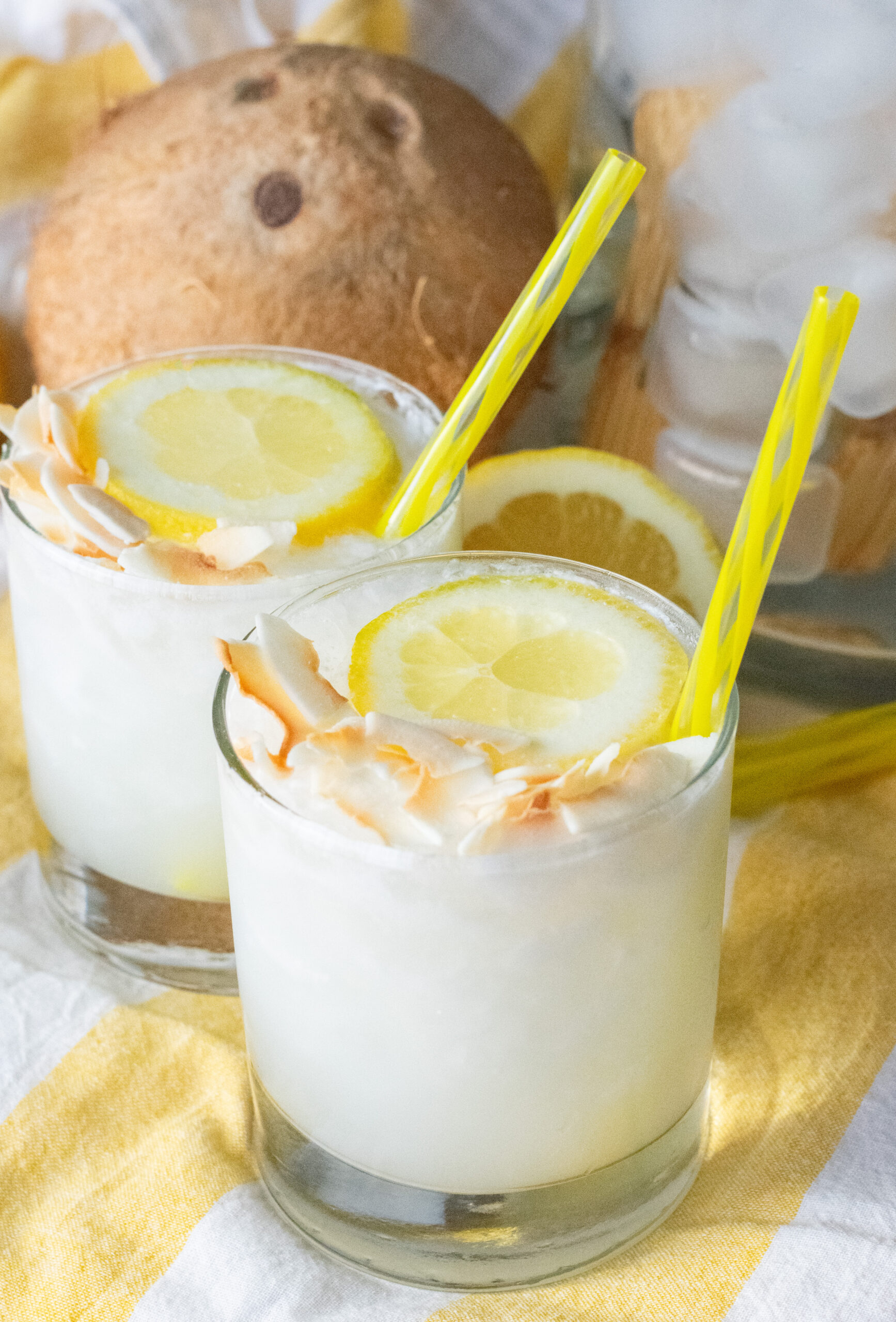 Two creamy Lemoncoco lemonade drinks with yellow straws, garnished with lemon slices and toasted coconut flakes