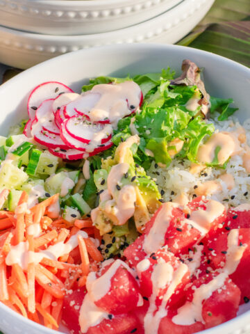 Fresh watermelon poke bowl with rice, avocado, and sesame seeds in a white bowl.
