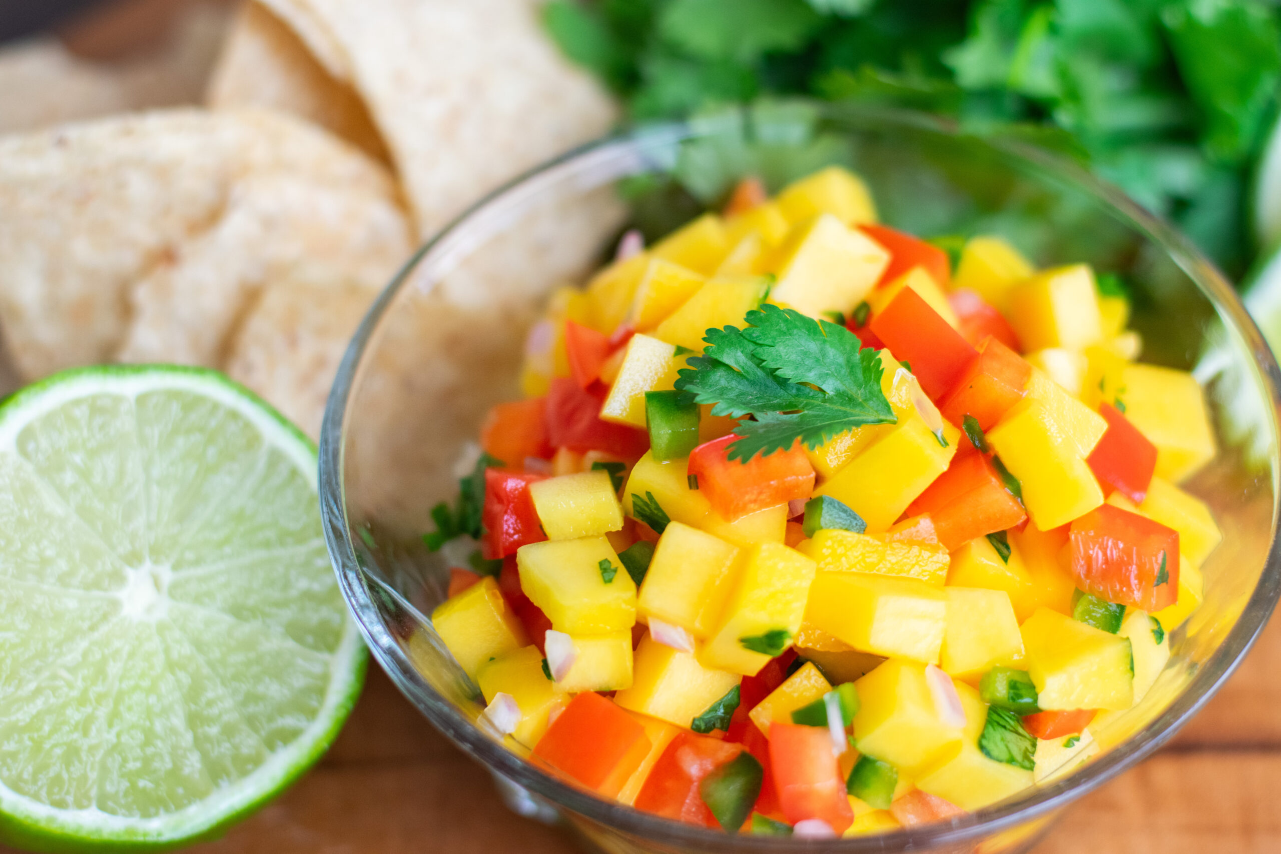 Colorful fresh mango salsa recipe with diced mango, onion, and jalapeño next to lime and tortilla chips