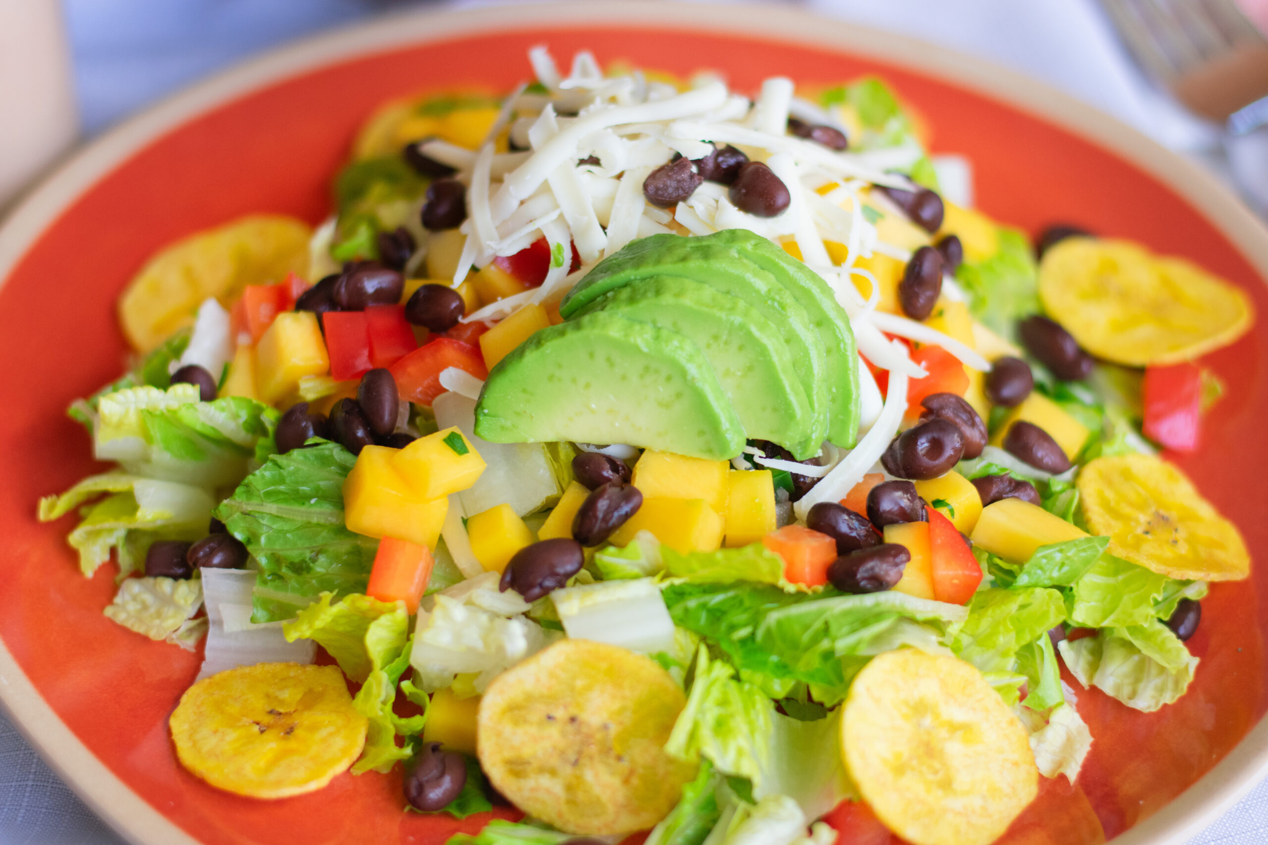 Overhead view of Mango Fiesta Salad in a large wooden bowl surrounded by toppings, fresh salsa, and dressing on the side.