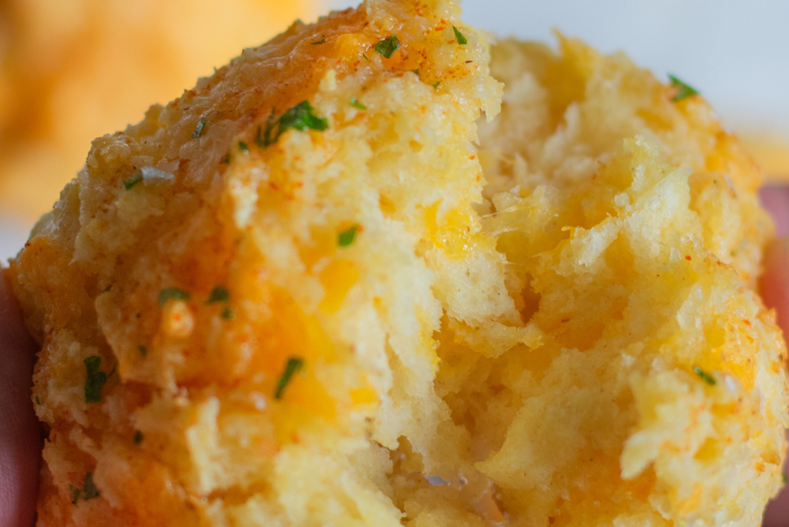 Golden homemade buttermilk cheddar biscuit broken open to show fluffy, cheesy interior, with steam rising and more biscuits blurred in the background.