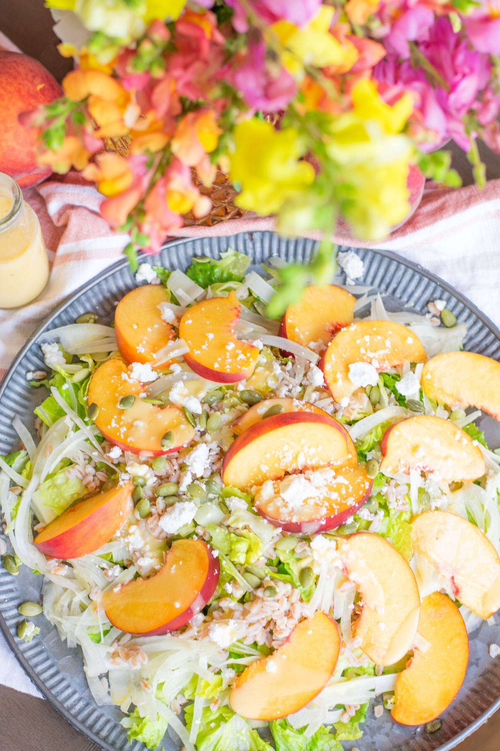 Overhead view of peach fennel salad with farro, ricotta salata, and hot honey peach nectar dressing, styled beside fresh flowers
