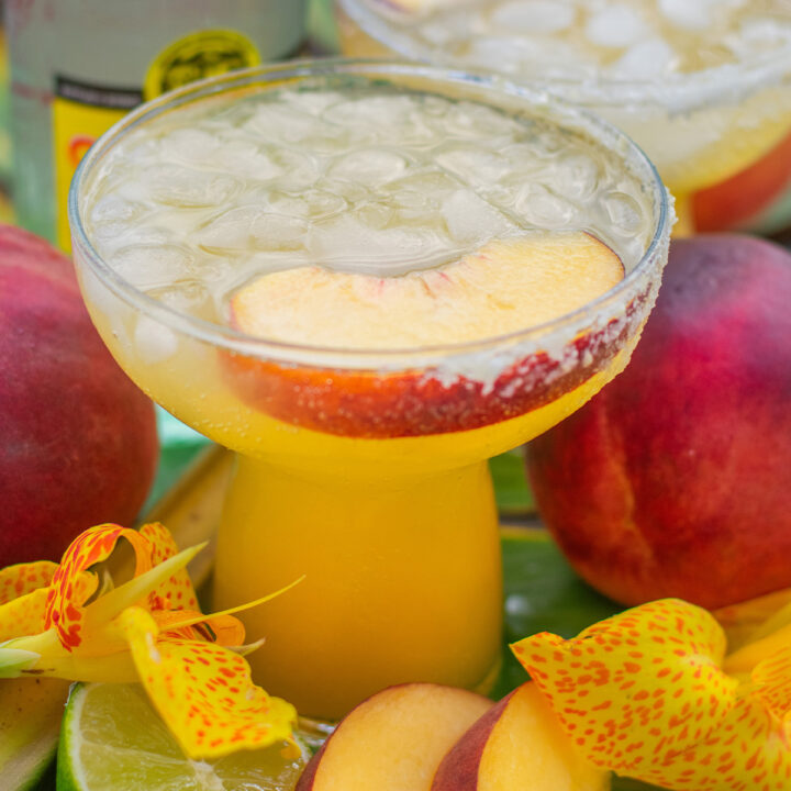Refreshing peach margarita in a glass rimmed with sugar, garnished with fresh peach slices and bubbles from Topo Chico.