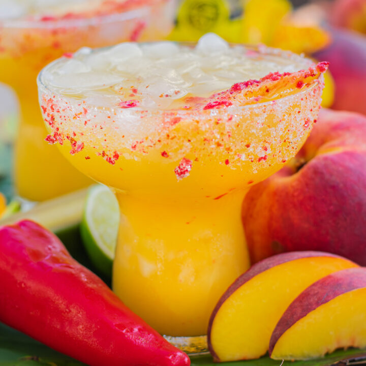 Spicy margarita recipe with hot honey, fresh peach, pepper garnish, and tajín rimmed glass