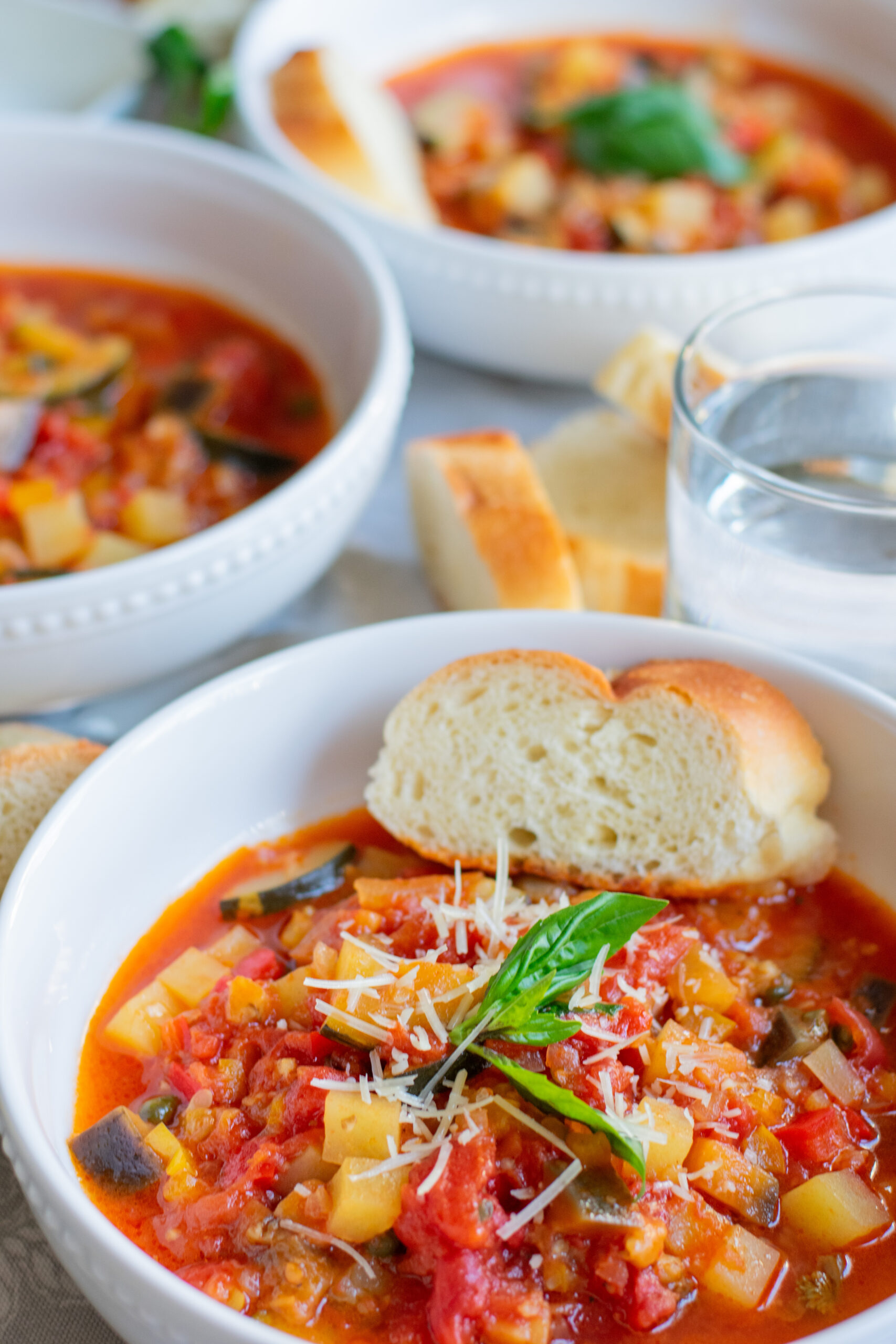 Bowl of Giambotta, Italian vegetable soup, served with bread and extra bowls in the background
