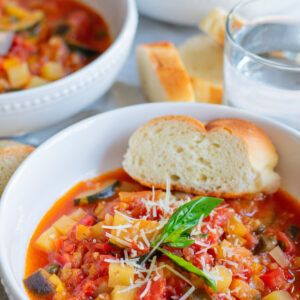 Bowl of Giambotta, an Italian vegetable soup, topped with Parmesan and basil, served with bread.