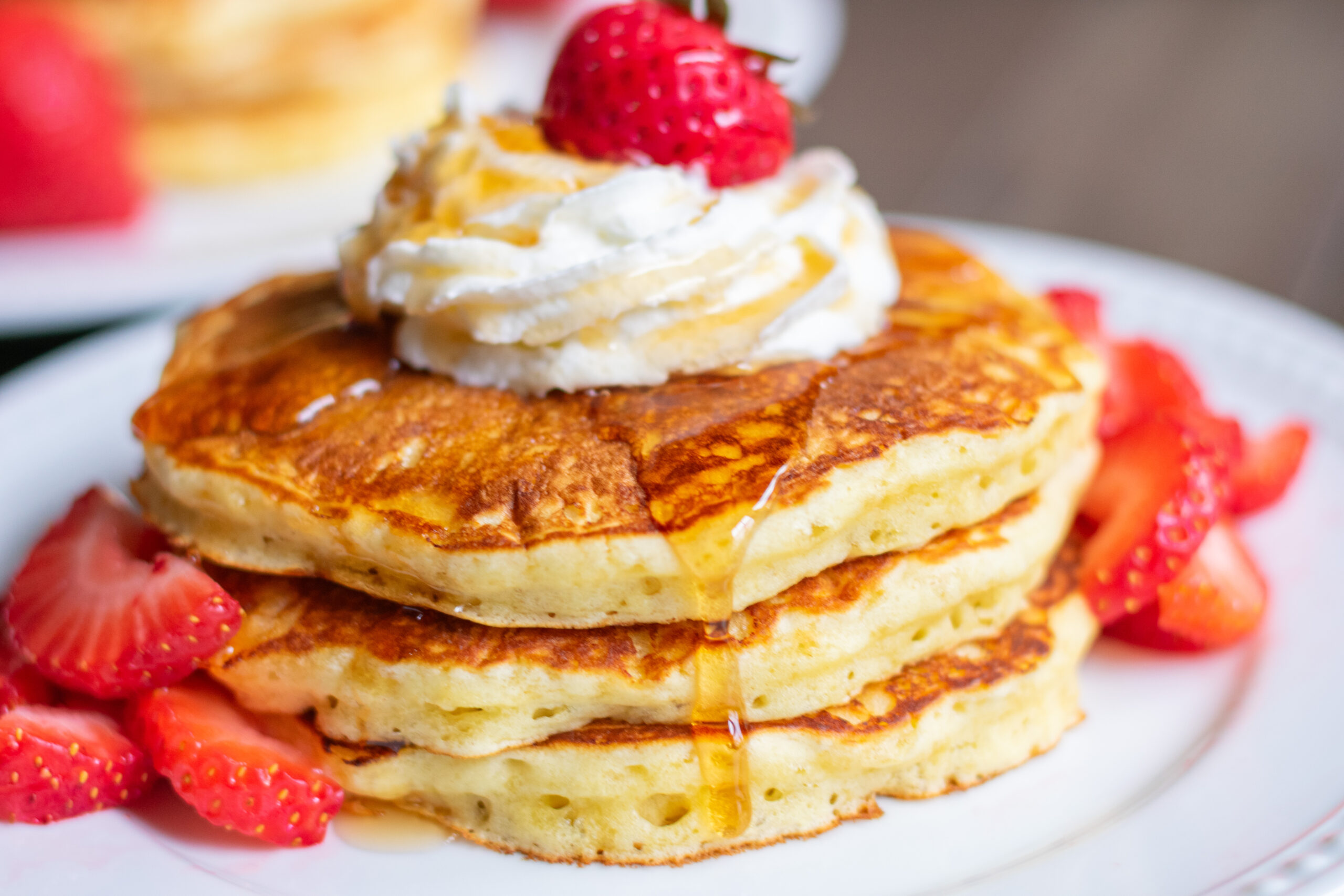 Maple syrup dripping slowly over a stack of fluffy pancakes.