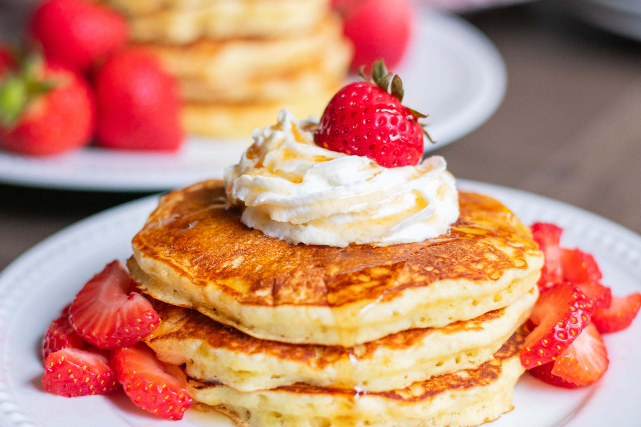 Stack of fluffy homemade pancakes with whipped cream and syrup drizzle.