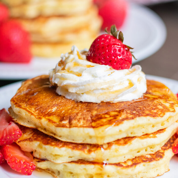 Fluffy pancakes recipe stacked with whipped cream and maple syrup