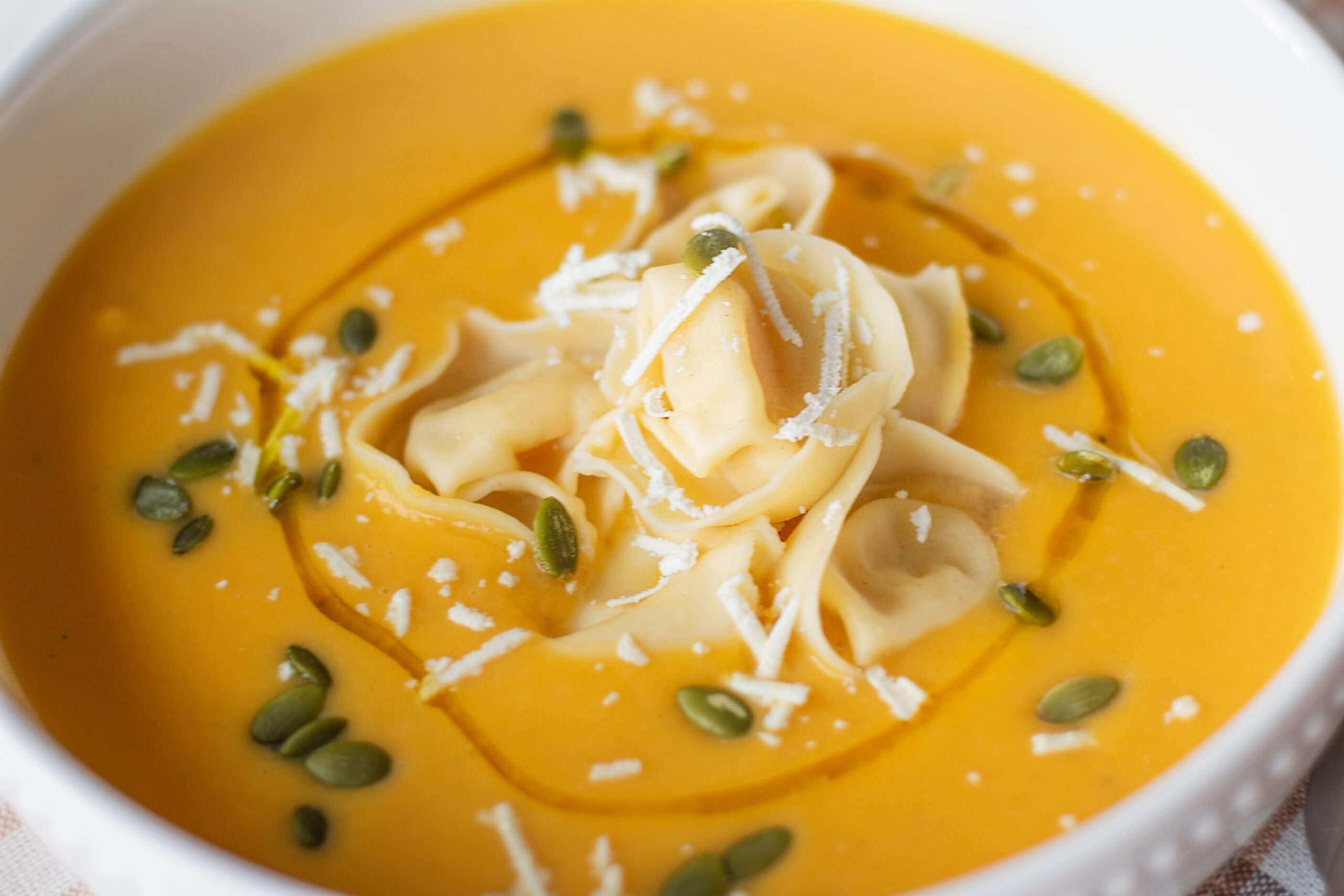 Overhead shot of roasted butternut squash soup with tortellini, toppings, and an olive oil drizzle.