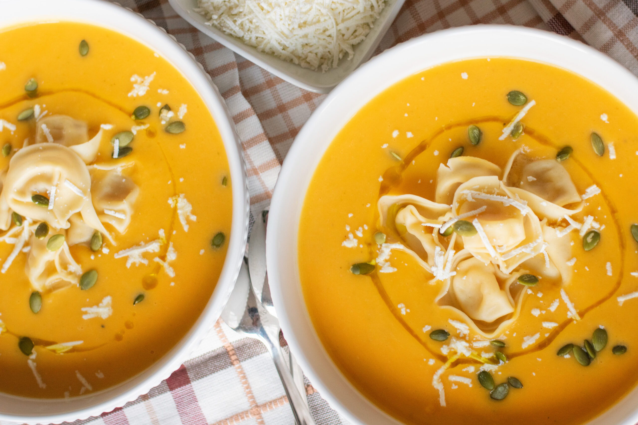 Overhead shot of two bowls of roasted butternut squash soup with tortellini and a small bowl of ricotta salata.