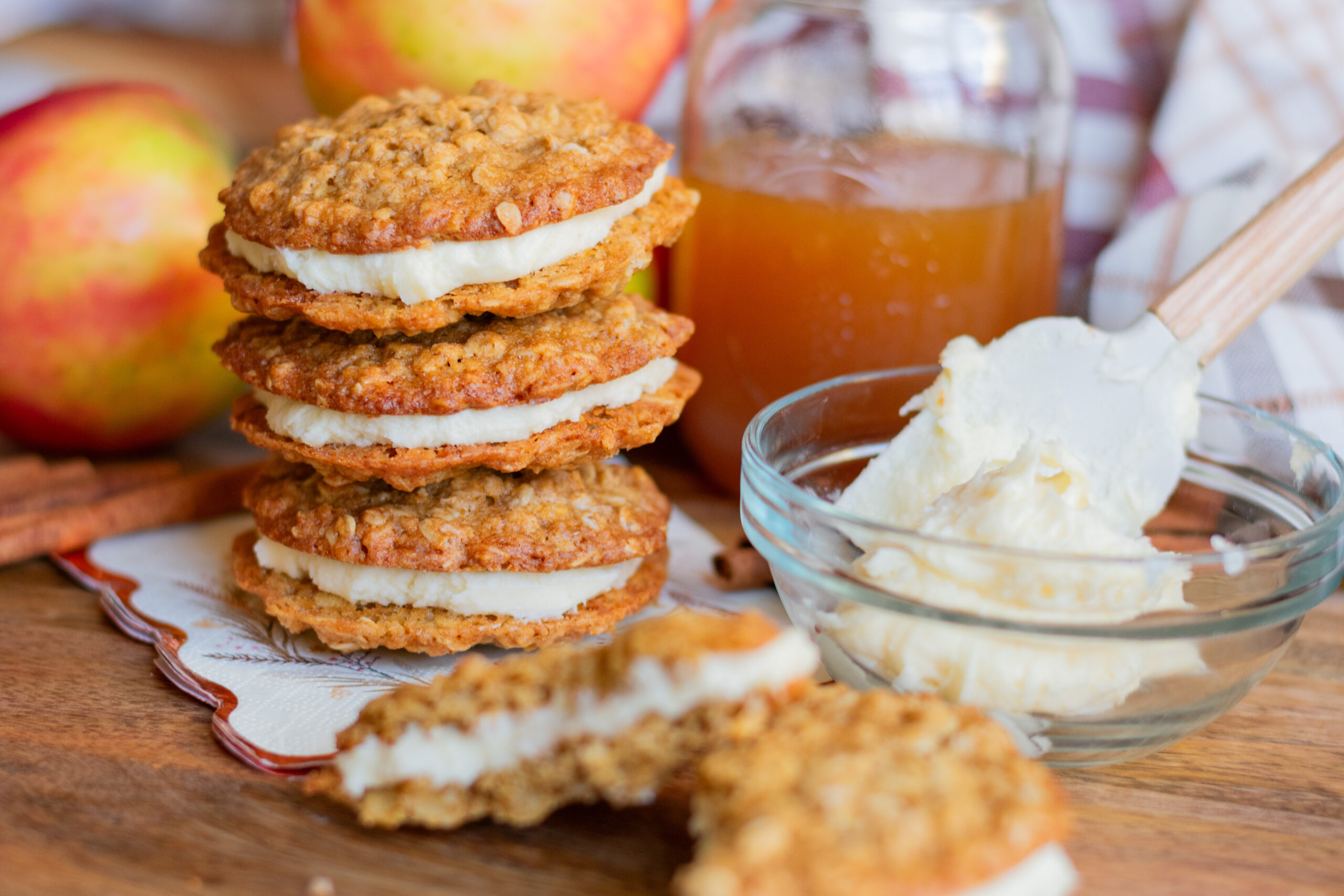 Apple cider oatmeal cream pies with soft oatmeal cookies, cream filling, apples, and apple cider on a baking surface