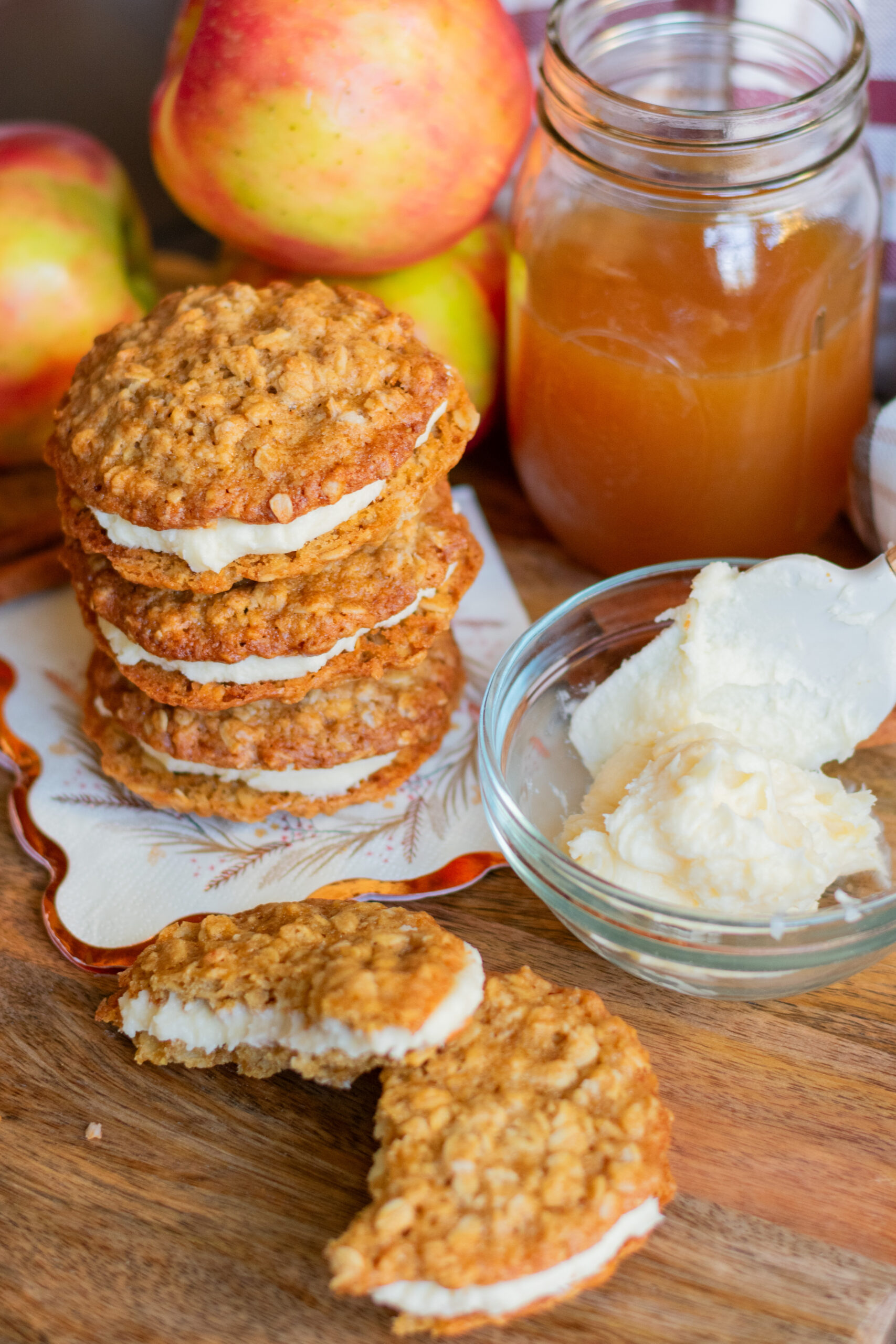 Apple cider oatmeal cream pies stacked beside fluffy frosting and a mason jar of apple cider