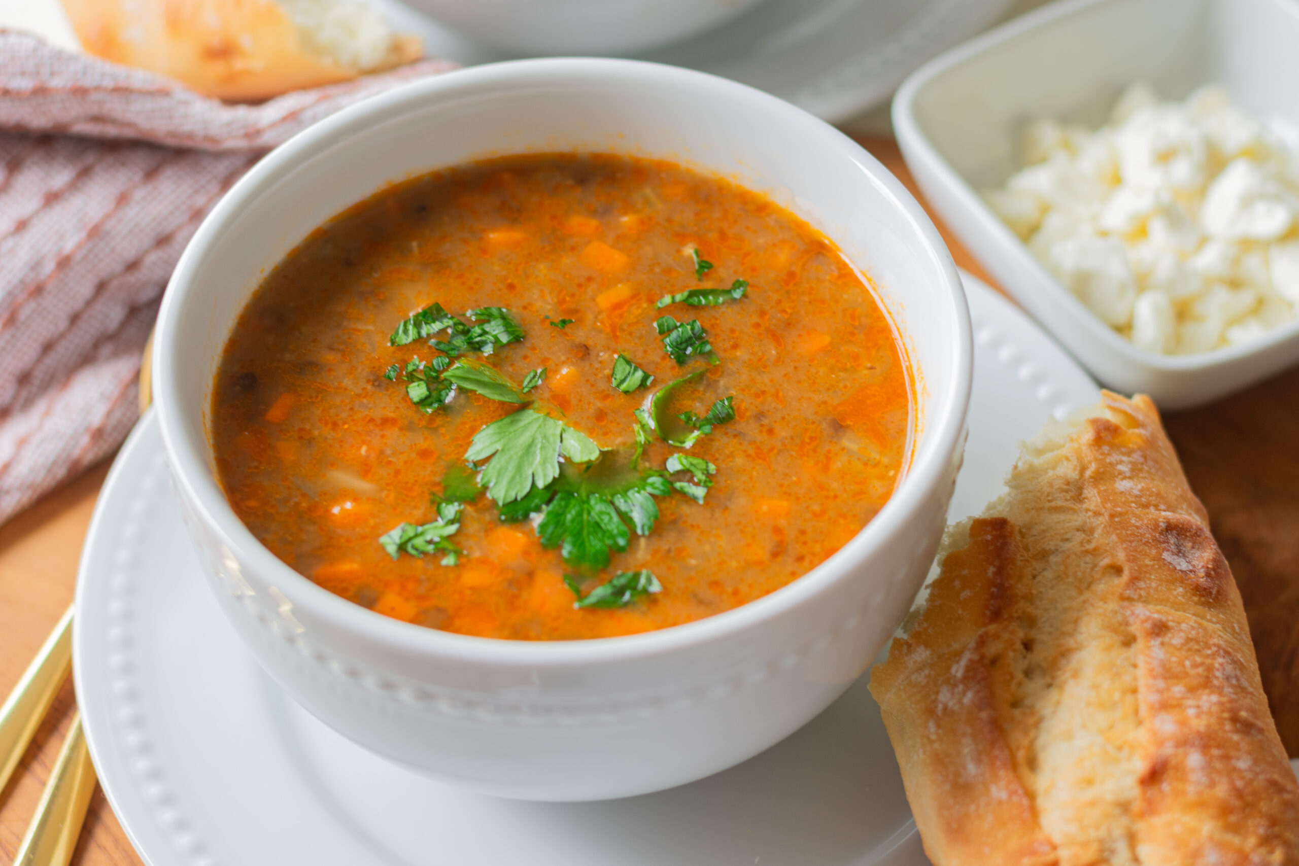 Bowl of hearty vegetarian lentil soup topped with feta cheese, served with crusty bread.