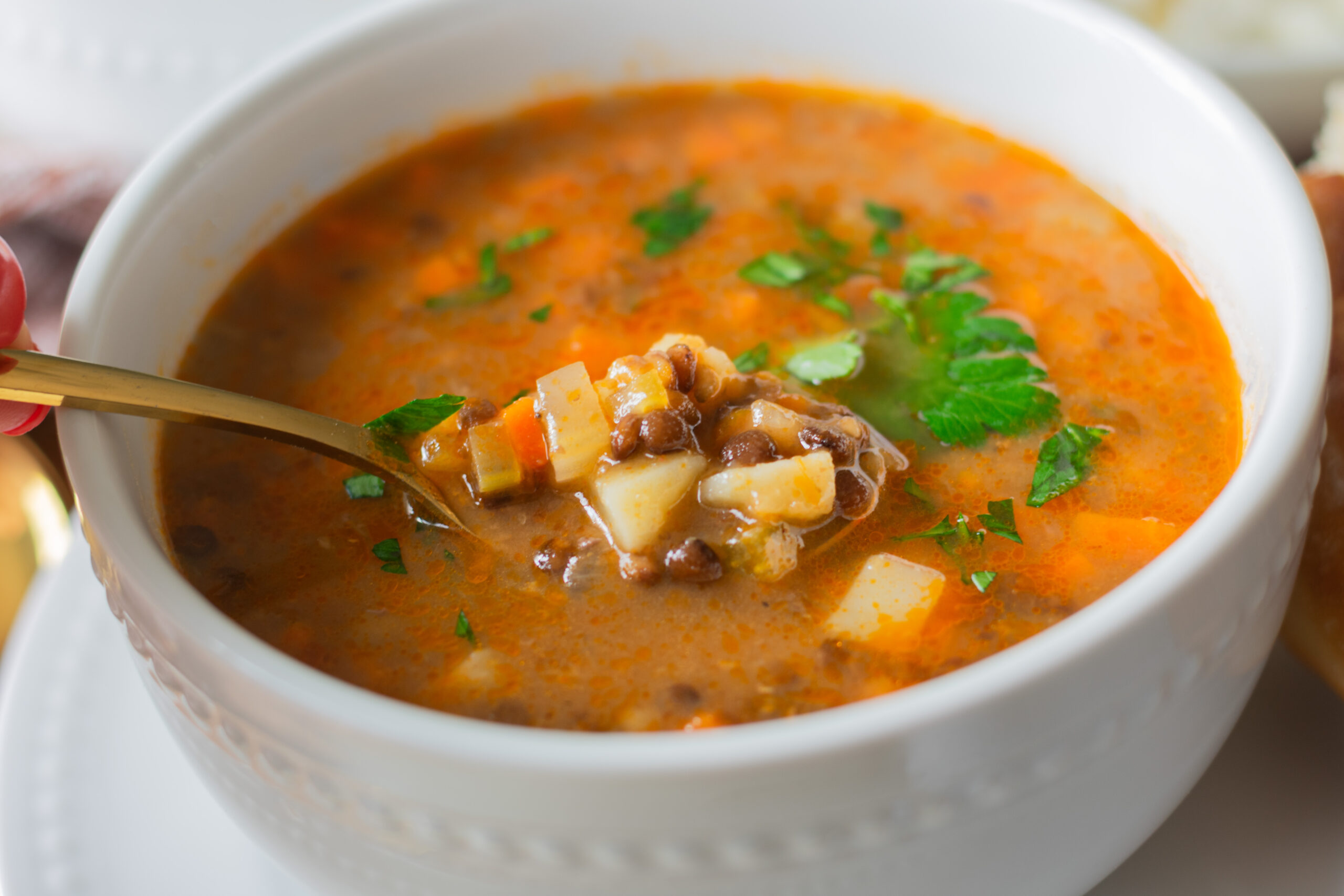 Close-up of a spoon lifting hearty vegetarian lentil soup with lentils and vegetables.