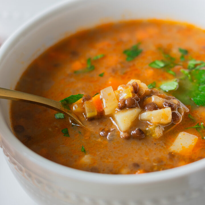 Spoon lifting a hearty vegetarian lentil soup with vegetables in a warm, broth-based bowl.