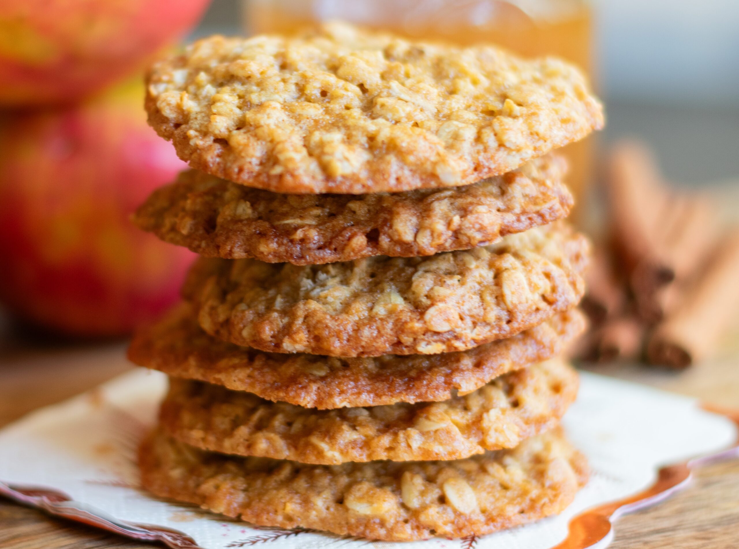 Zoomed into stacked apple cider oatmeal cookies styled with fresh apples and apple cider