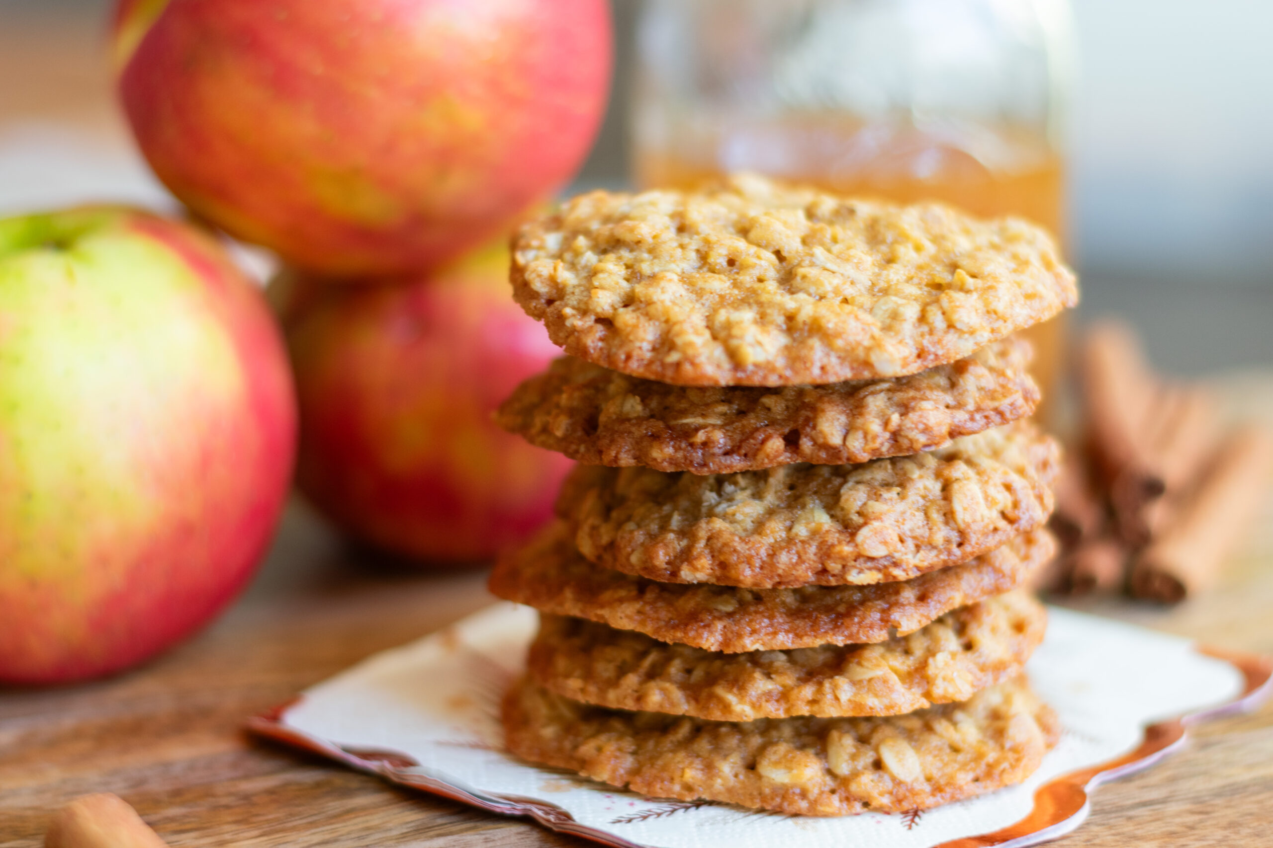 Stacked apple cider oatmeal cookies styled with fresh apples and apple cider
