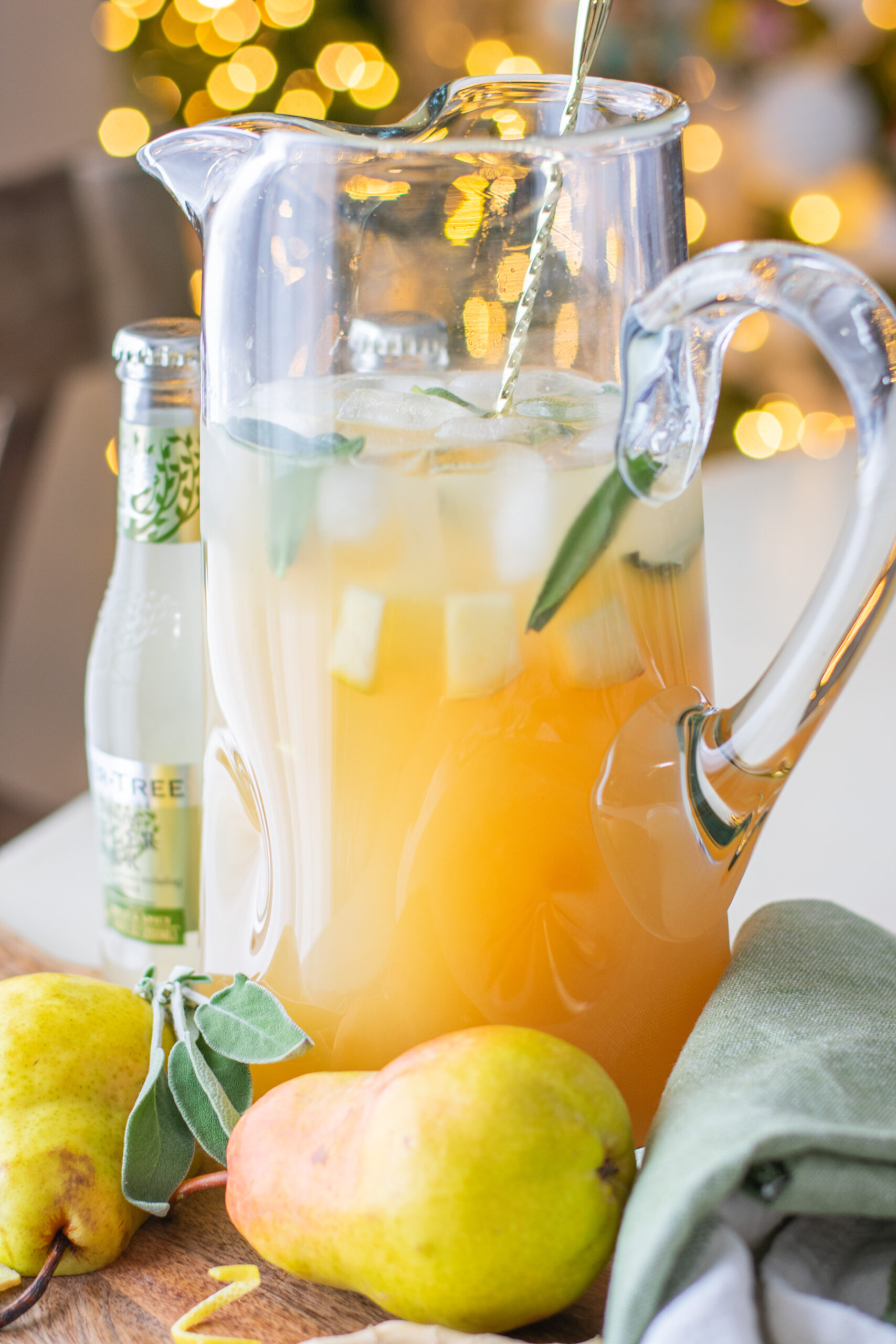 Sage pear drink batched in a glass pitcher with fresh sage, pear, and ice for entertaining