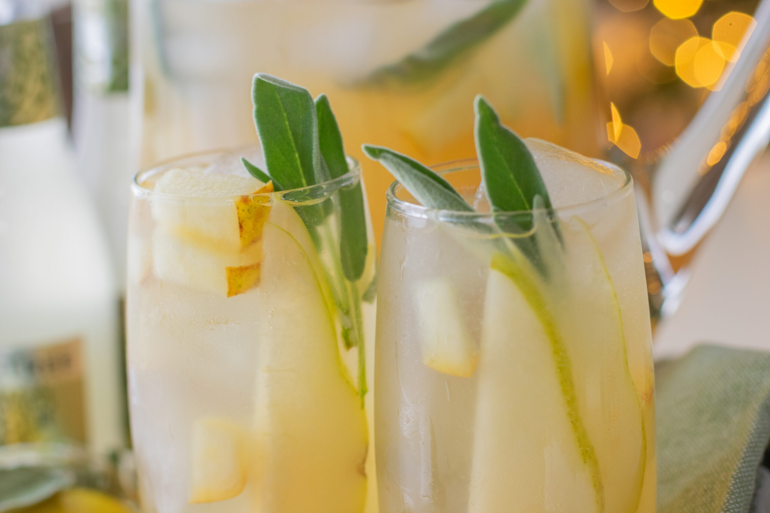 Two sage pear drinks served over ice, garnished with fresh sage and pear slices