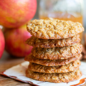 Stacked apple cider soft oatmeal cookies near apple cider and fresh apples