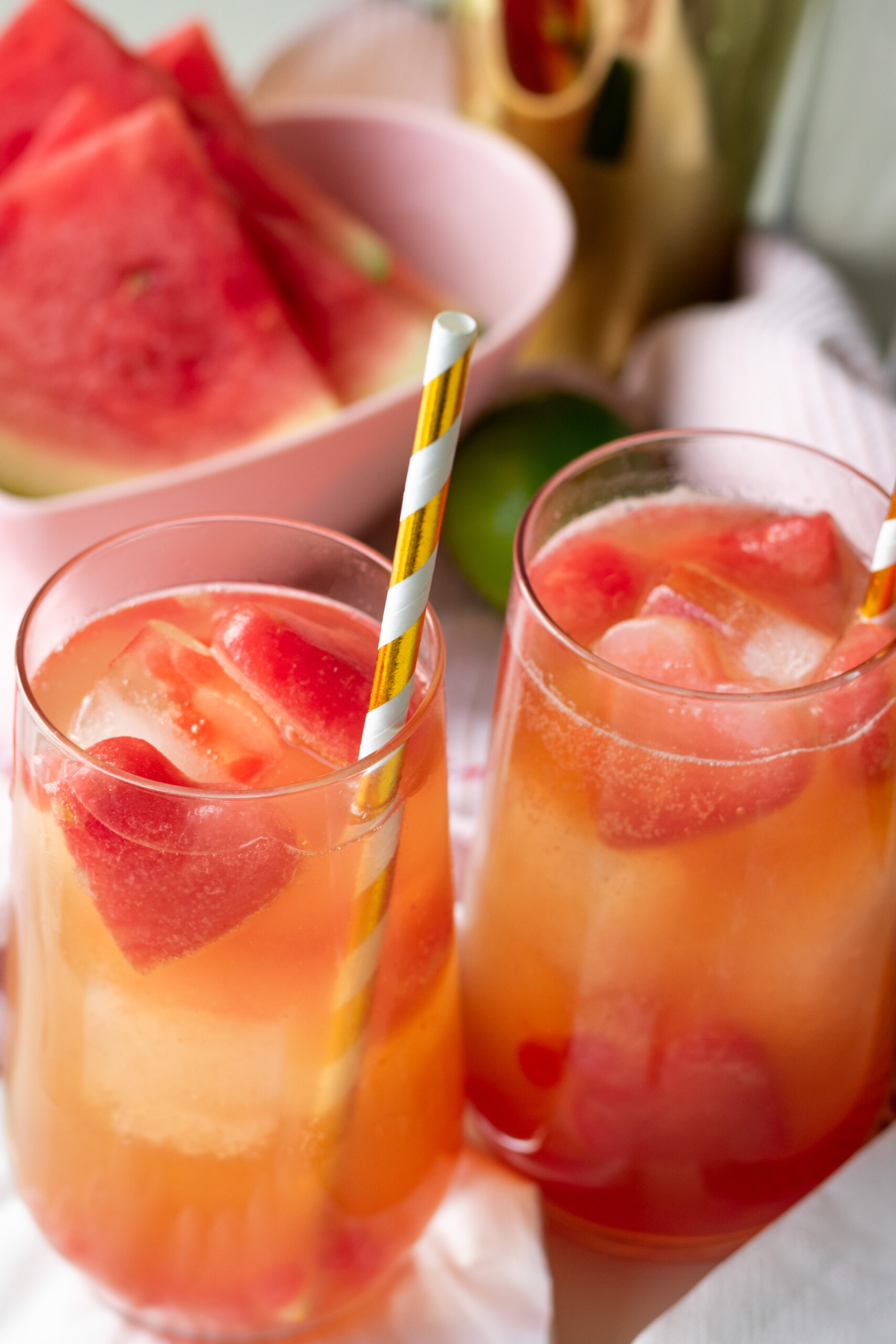 Two tall glasses of strawberry popping boba mocktail with watermelon ice hearts, layered pink and red fruit drink photographed overhead on a light surface