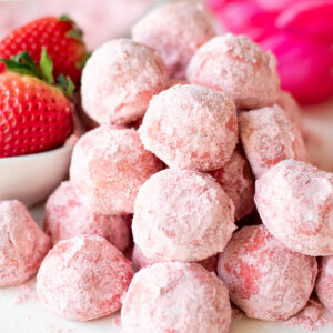 stacked strawberry snowball cookies with strawberries in background