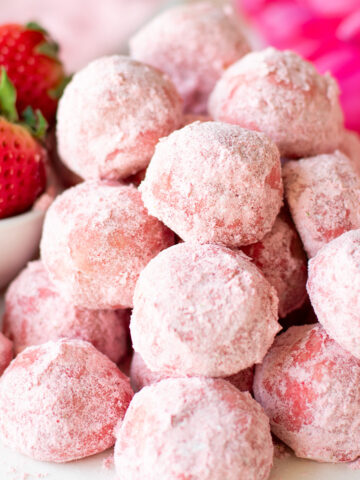 stacked strawberry snowball cookies with strawberries in background