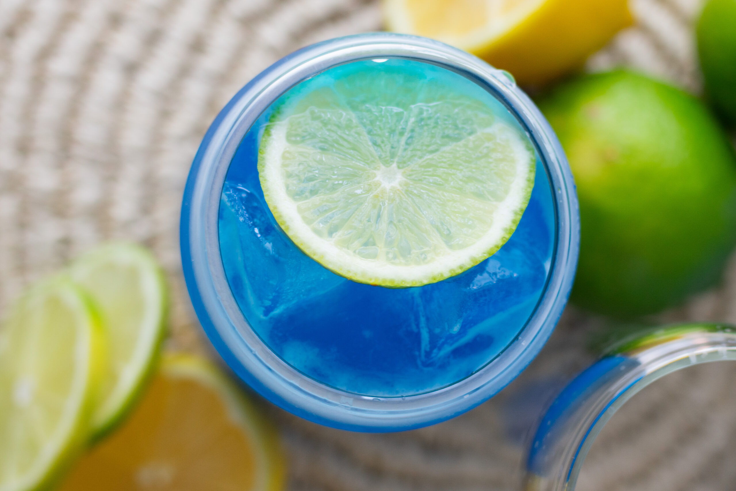 Overhead view of a Blue Ocean Water Drink Recipe with lime wheels, ice, and optional coconut sea foam.