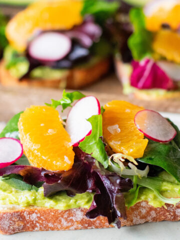 Avocado toast topped with dressed greens, mandarin oranges, radishes, and citrus vinaigrette