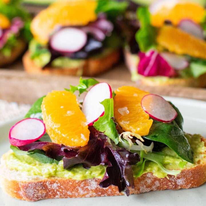 Avocado toast topped with dressed greens, mandarin oranges, radishes, and citrus vinaigrette