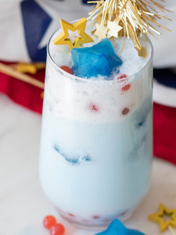 Red white and blue patriotic mocktail with strawberry popping boba, coconut milk, blue spirulina star ice cubes, and sparkling soda.